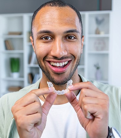 Smiling man holding an Invisalign aligner