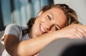Woman laying on couch smiling after visiting cosmetic dentist in Belmont, MA