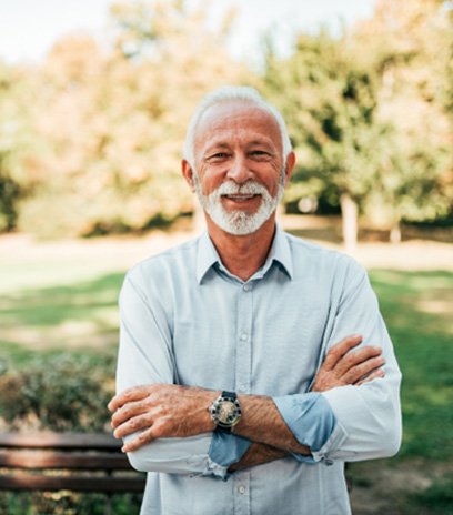 Senior man in park smiling with arms folded