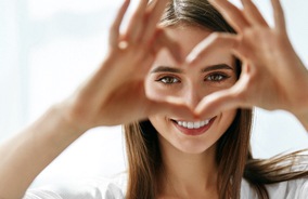 Woman smiling and making heart shape with hands after eye exam in Belmont, MA
