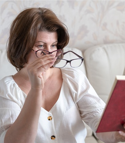 Woman with presbyopia using reading glasses over regular glasses to see