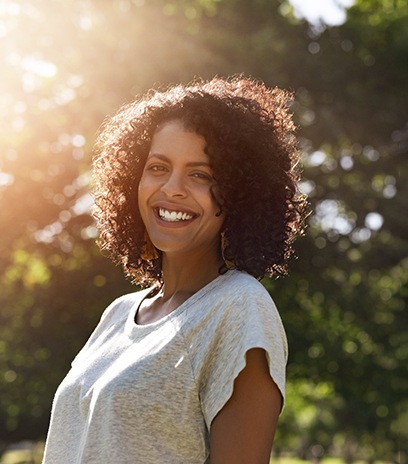 Woman in light grey shirt outside and smiling