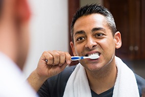 Man with towel around neck brushing his teeth