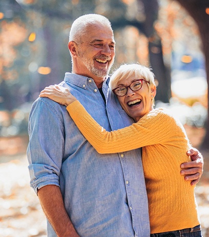 An older couple with dental implants in Belmont smiling outside.