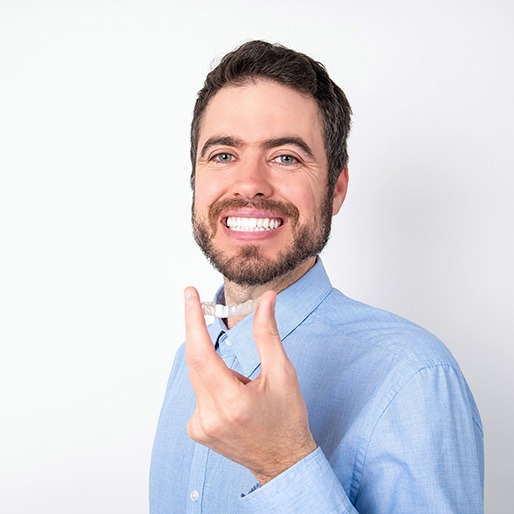Bearded man holding Invisalign aligner and smiling
