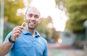 Man in blue collared shirt holding Invisalign aligner