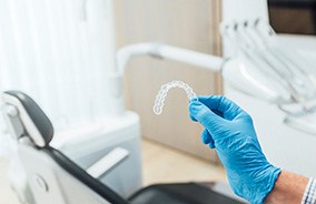 Gloved hand holding Invisalign aligner in dentist’s office