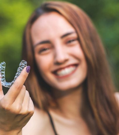 Woman holding an aligner for Invisalign in Belmont, MA