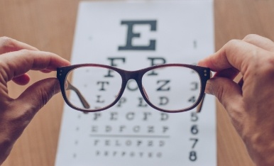 Hand holding a pair of eyeglasses over an eye exam chart