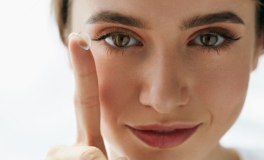 Closeup of woman's face and a contact lens on her finger tip