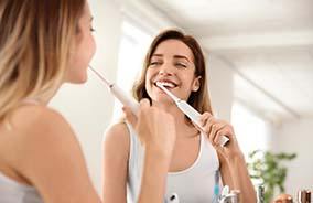 Woman smiling and brushing her teeth in mirror