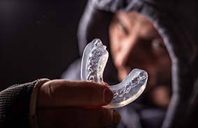 Man in hoodie holding an athletic mouthguard