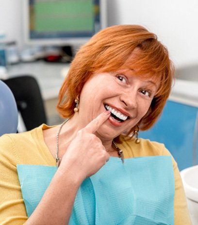 Red-haired woman in dental chair pointing to smile