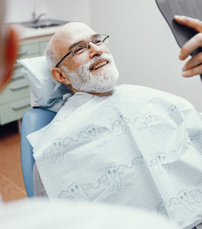 Man smiling in handheld mirror at the dentist
