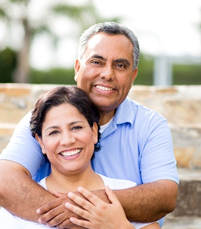 An older couple smiling and hugging outside.